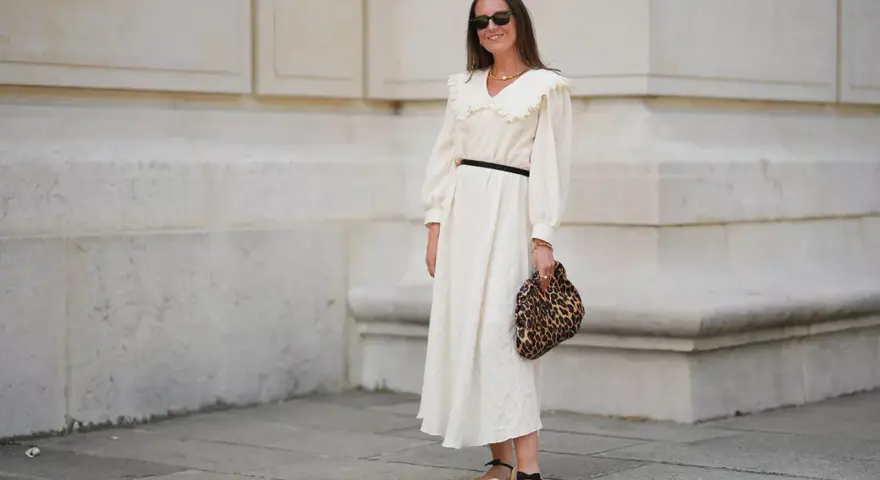 Kobieta w kremowej sukience z falbankowym kołnierzem, czarnym paskiem i panterkową kopertówką. Uosobienie swobodnej elegancji smart casual damski.