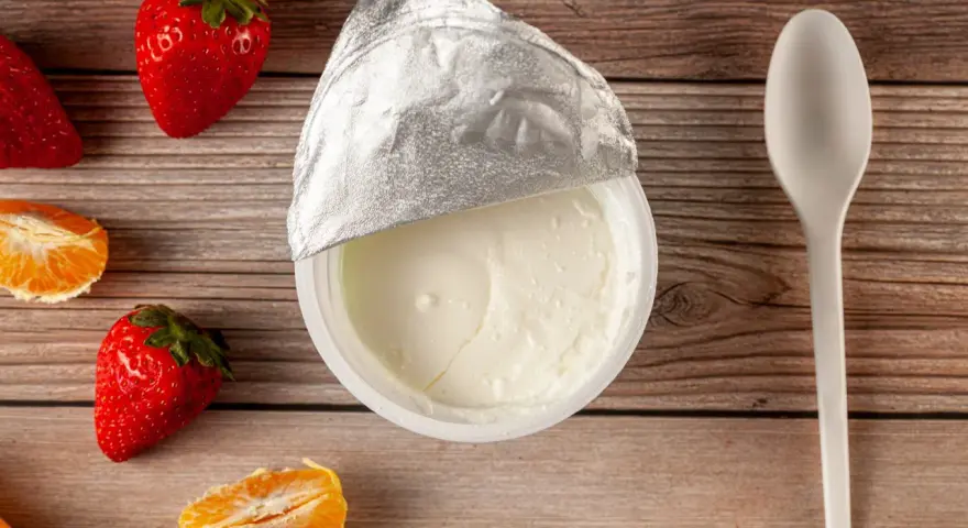 Jogurt naturalny właściwości: kremowy, gładki, z owocami i łyżeczką na drewnianym tle. Idealny na zdrowy deser.
