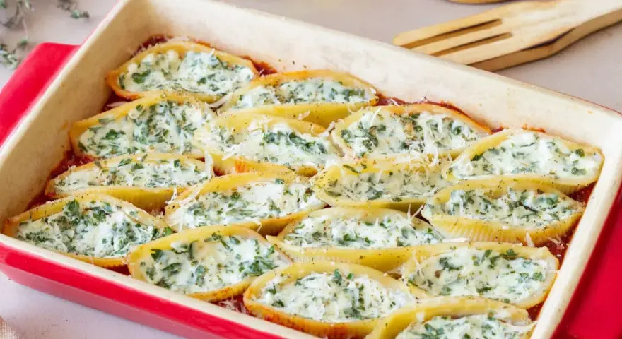Pyszne muszle ze szpinakiem i ricottą, zapieczone w sosie pomidorowym, posypane parmezanem.