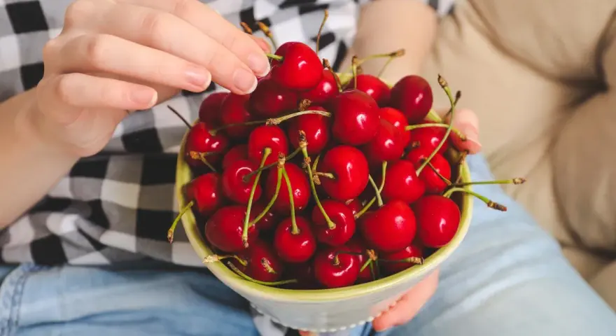 Ręce trzymają miseczkę pełną soczystych, czerwonych czeresni. Idealna przekąska na keto!