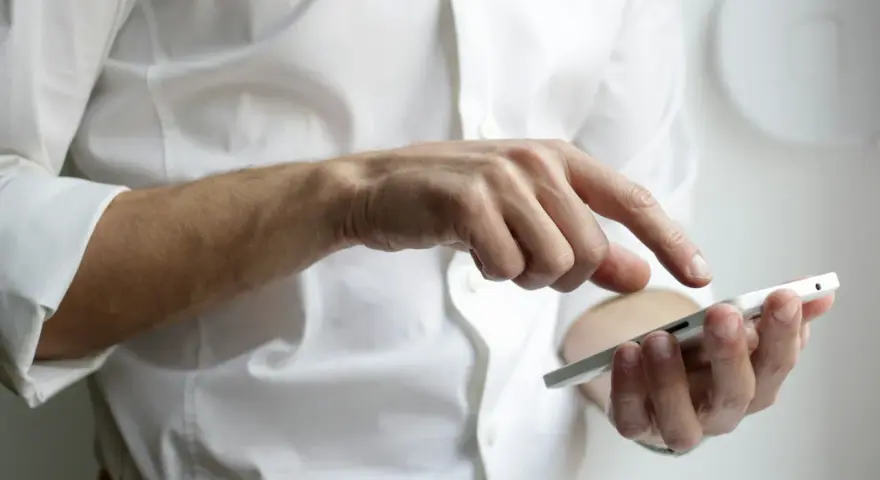 Mężczyzna w białej koszuli używa smartfona, czując narastający ból głowy od telefonu.