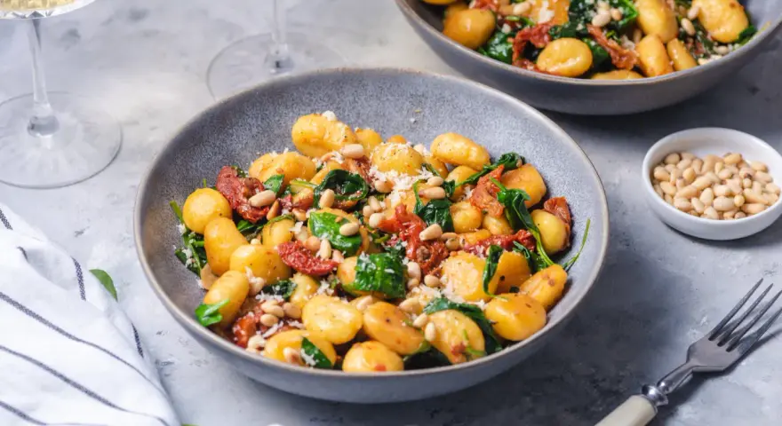Pyszne gnocchi z pomidorami, szpinakiem i orzeszkami pinii, posypane parmezanem. Idealne danie na szybki obiad.