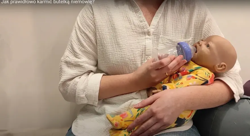 Instrukcja jak prawidłowo karmić butelką niemowlę. Pokazano karmienie lalki-niemowlaka.