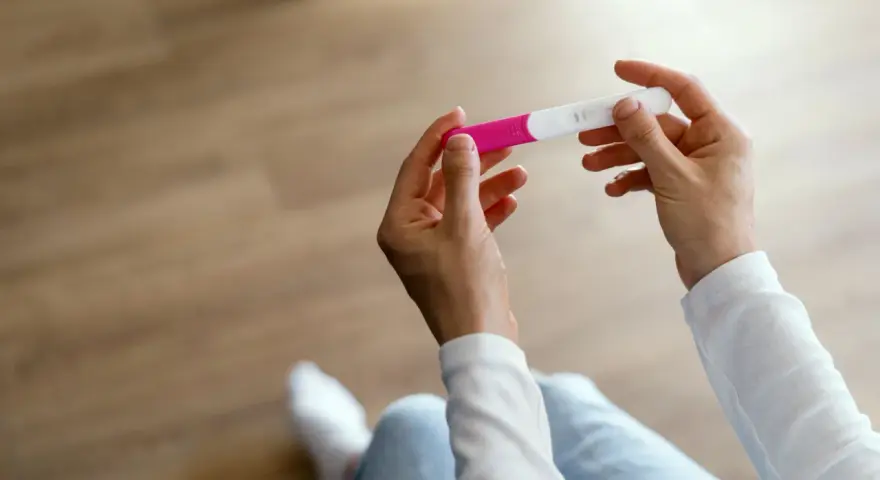 Dłonie trzymające test ciążowy, który może wskazać pierwsze objawy ciąży.