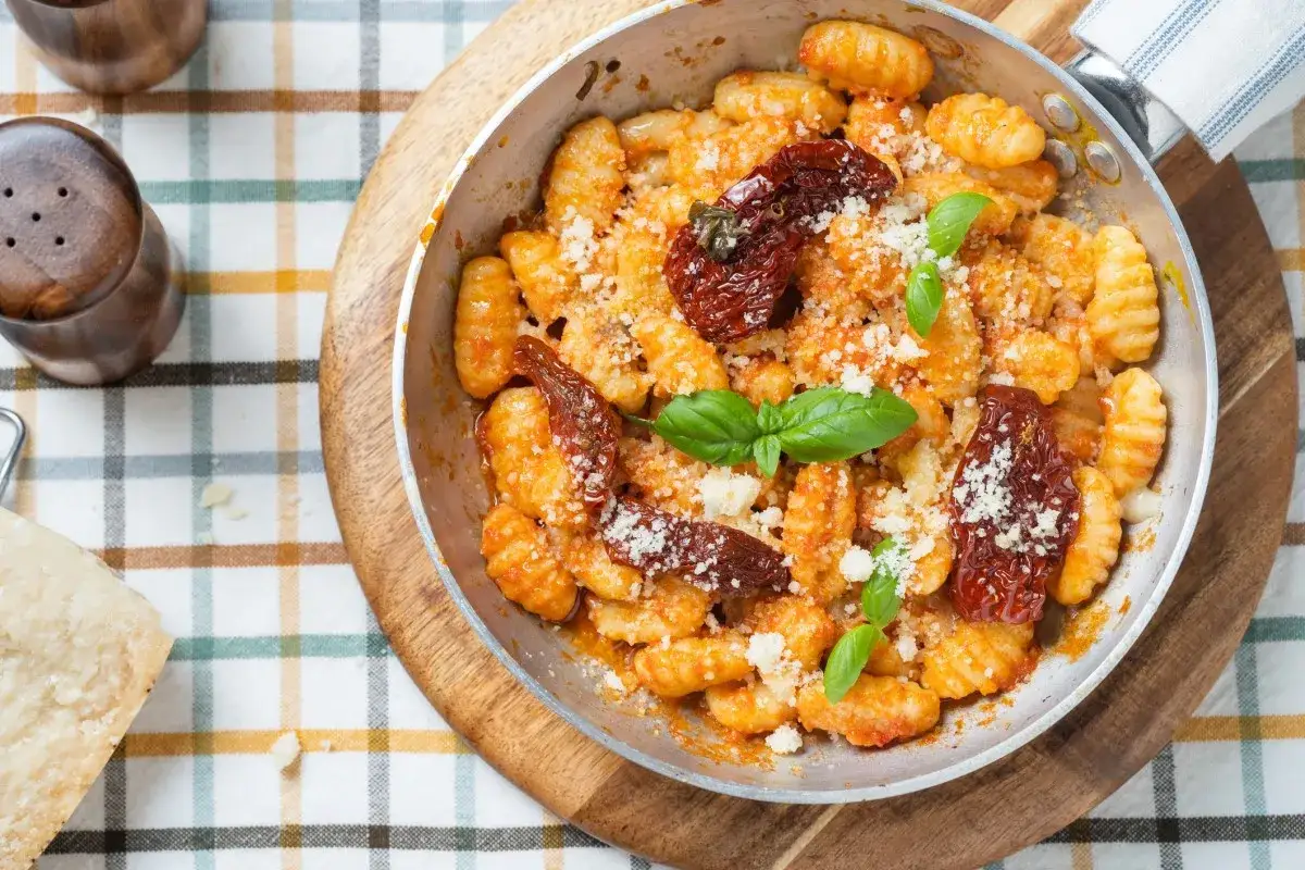 Pyszne gnocchi z pomidorami, posypane parmezanem i udekorowane bazylią. Danie podane w metalowej patelni na kratkowanym obrusie.