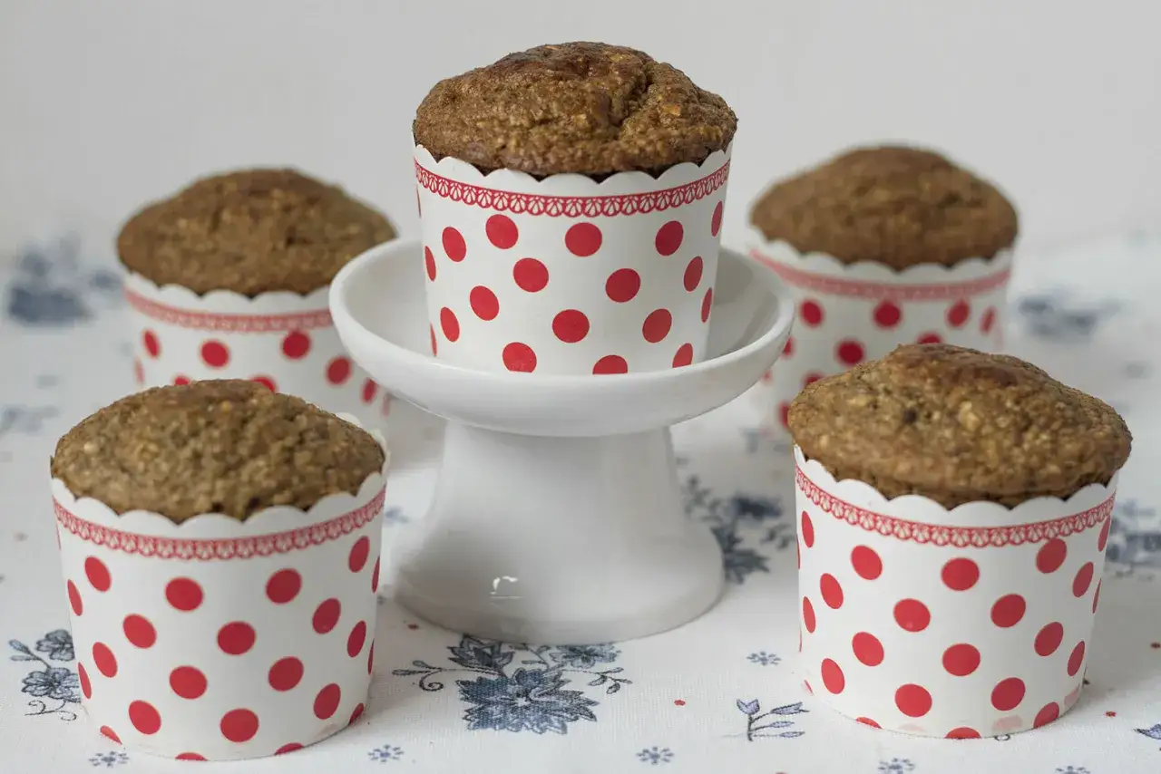 Pięć muffinek bananowych fit w papierowych foremkach w czerwone kropki, jedna na białej paterce.