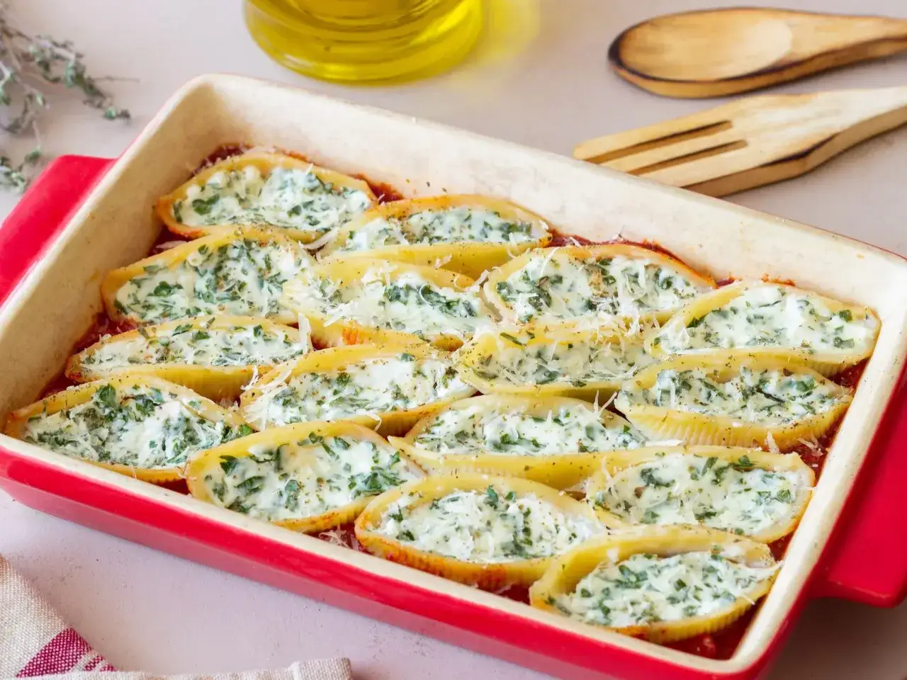 Muszle ze szpinakiem i ricottą, zapieczone w sosie pomidorowym, posypane parmezanem. Pyszne danie gotowe do podania.