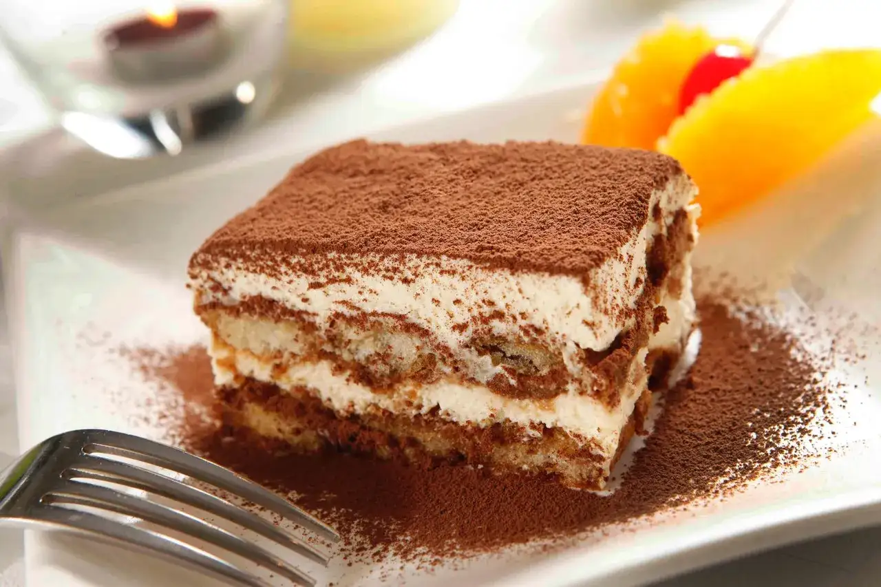 Pyszne tiramisu ze skyrem, posypane kakao, z owocami i widelcem na talerzu.