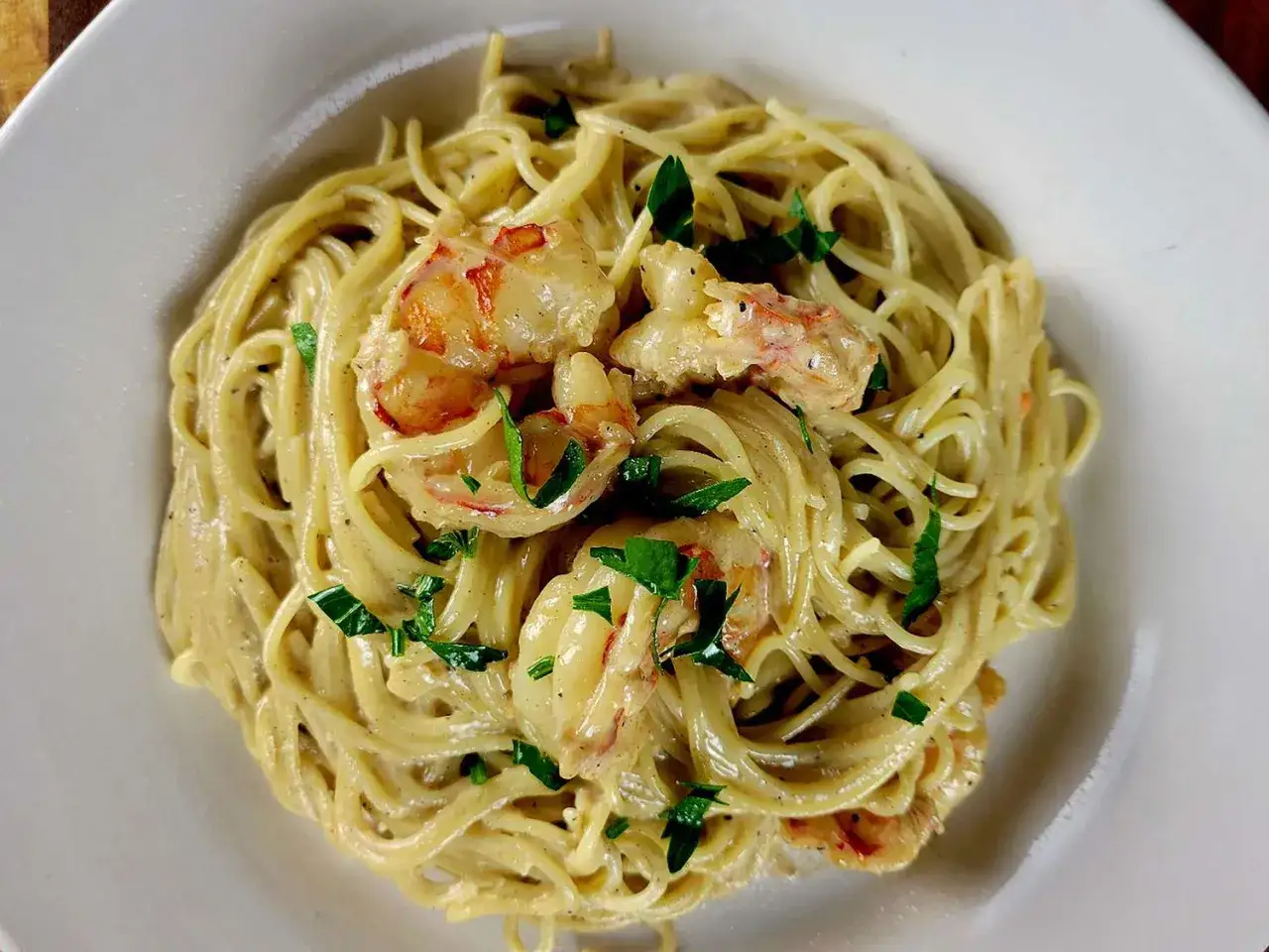 Pyszny przepis na krewetki w sosie śmietanowym z makaronem spaghetti, posypane natką pietruszki.