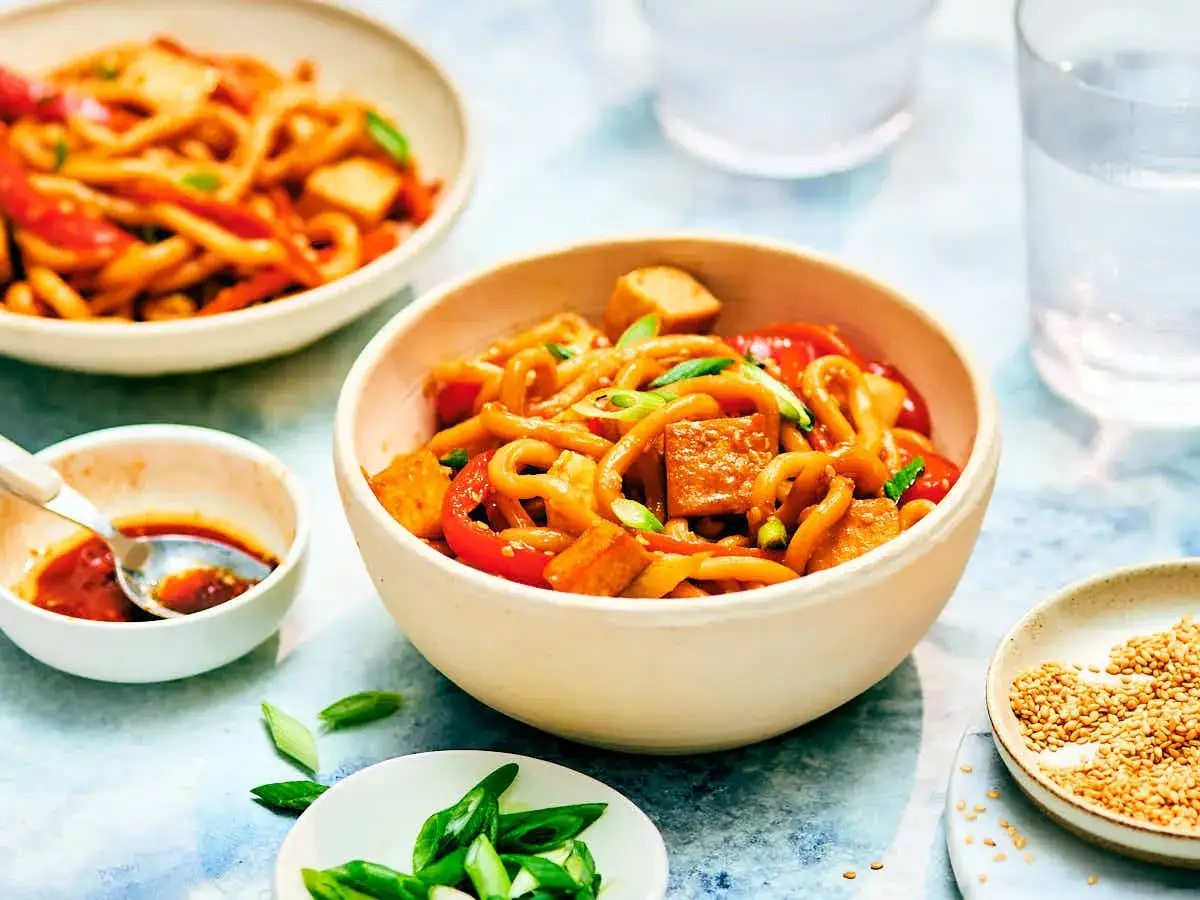 Pyszne danie z makaronem udon, kawałkami smażonego tofu, papryką i szczypiorkiem.
