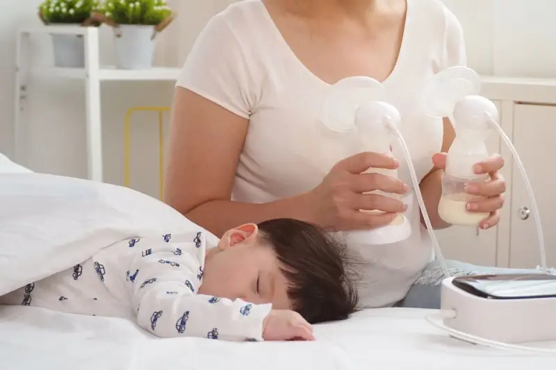 Mama odciąga pokarm 7-5-3, podczas gdy jej dziecko śpi spokojnie.